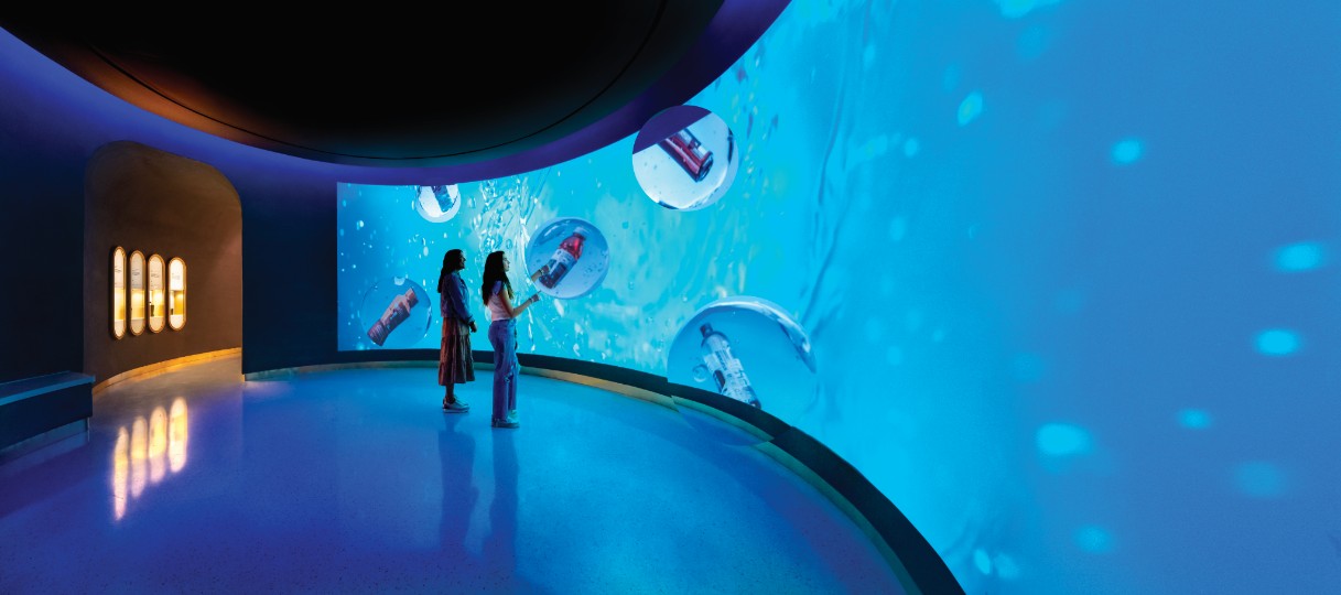 Visitors dwarfed by the underwater wall, bottles adrift in bubbles